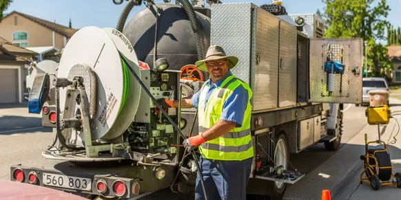 Worker operating sewer cleaning truck on street.