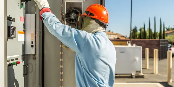 Worker operating electrical panel with safety gear.