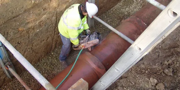 Worker cutting large pipe in trench.