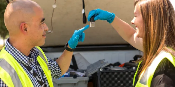 Two people examining a small vial outdoors.